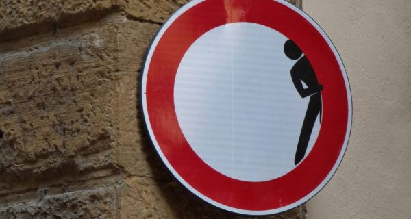 This picture showa a road sign - not allowed to enter the roas. But not the typical one , there a person hiding inside th sign, looking like hiding.