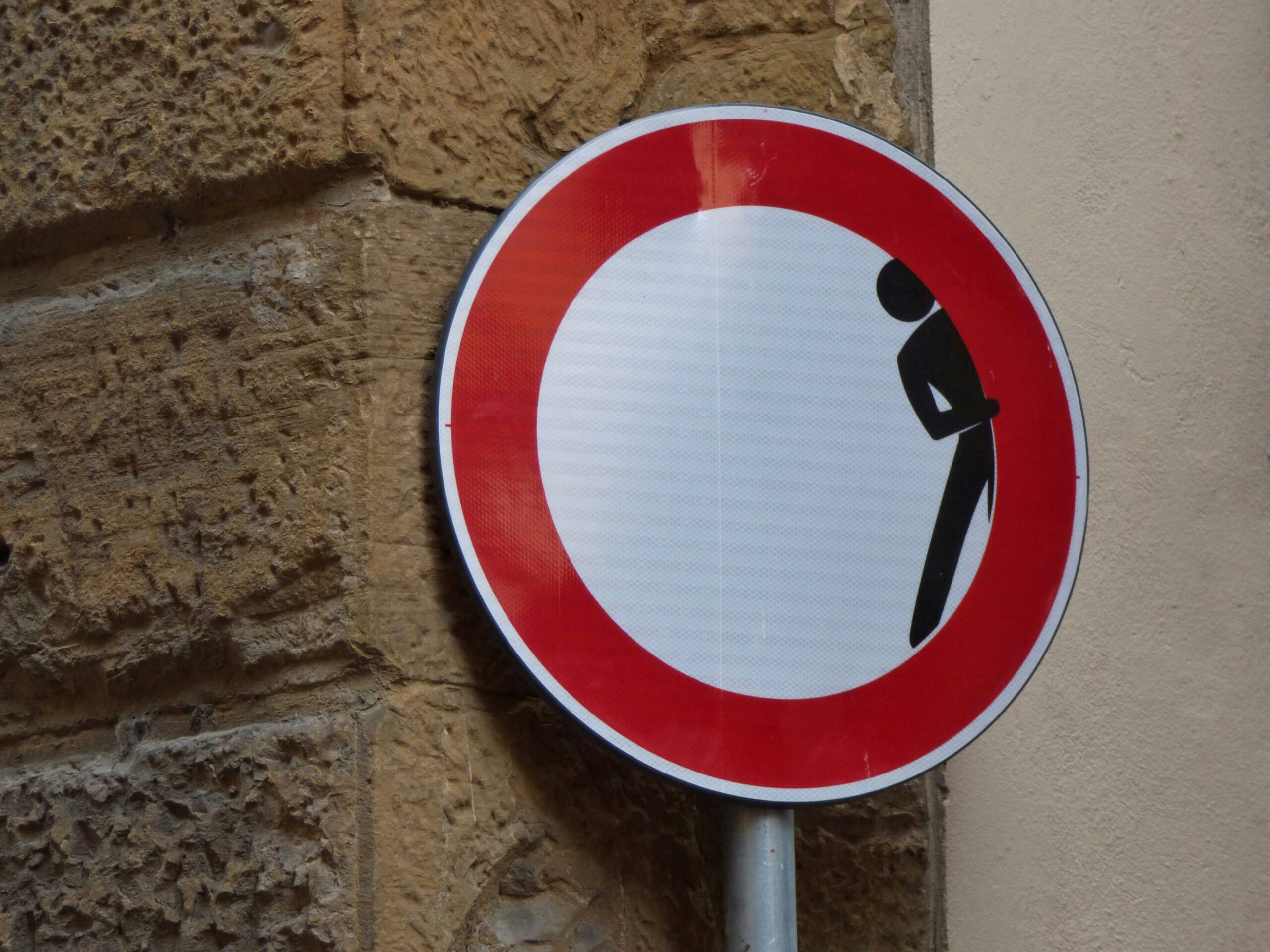This picture showa a road sign - not allowed to enter the roas. But not the typical one , there a person hiding inside th sign, looking like hiding.