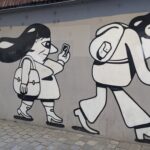 Graffiti auf der Mauer in einer Stadt in Frankreich - es sind Menschen in ihrem Alltag dargestellt, wie sie mit dem Handy laufen, Kinderwagen schieben