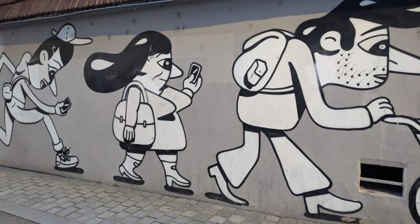 Graffiti auf der Mauer in einer Stadt in Frankreich - es sind Menschen in ihrem Alltag dargestellt, wie sie mit dem Handy laufen, Kinderwagen schieben